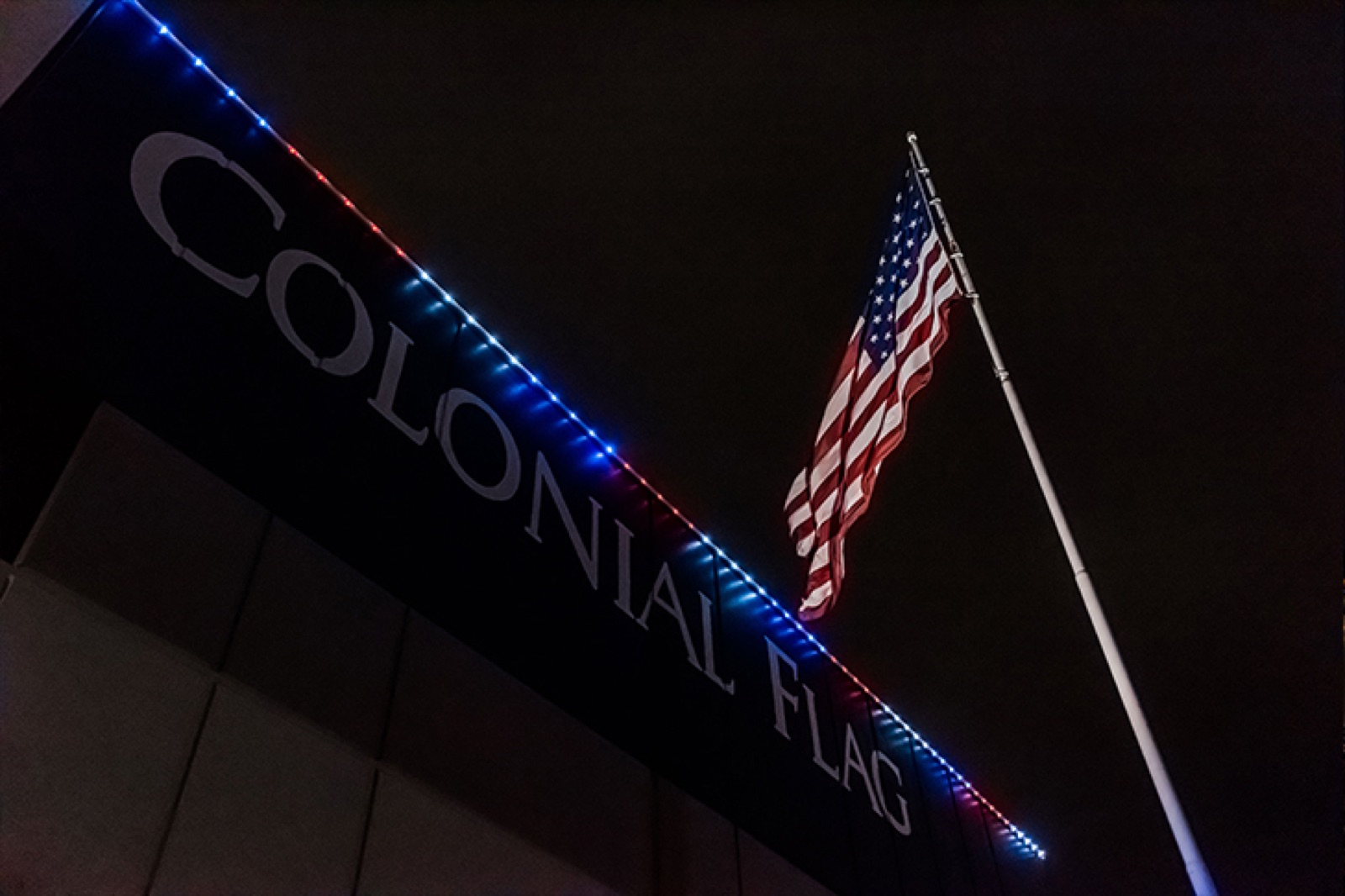 Red white and blue lighting on a commercial roofline beside an American flag