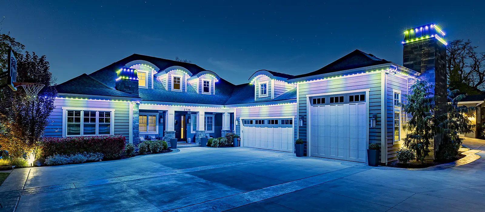 Wide residential home with blue and white permanent lighting